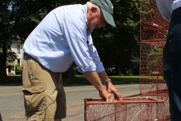 An older white man leans over a crab cage.