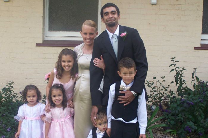 Daniel wears a suit with a pink flower in the lapel, with a woman in a formal dress, and three little girls, arms around a boy.