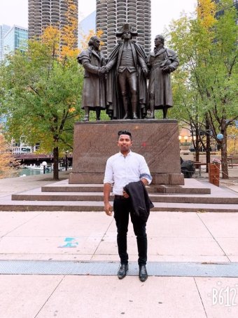 Rohingya refugee now resettled in Chicago A man stands in front of a statue of three men in a park in Chicago.